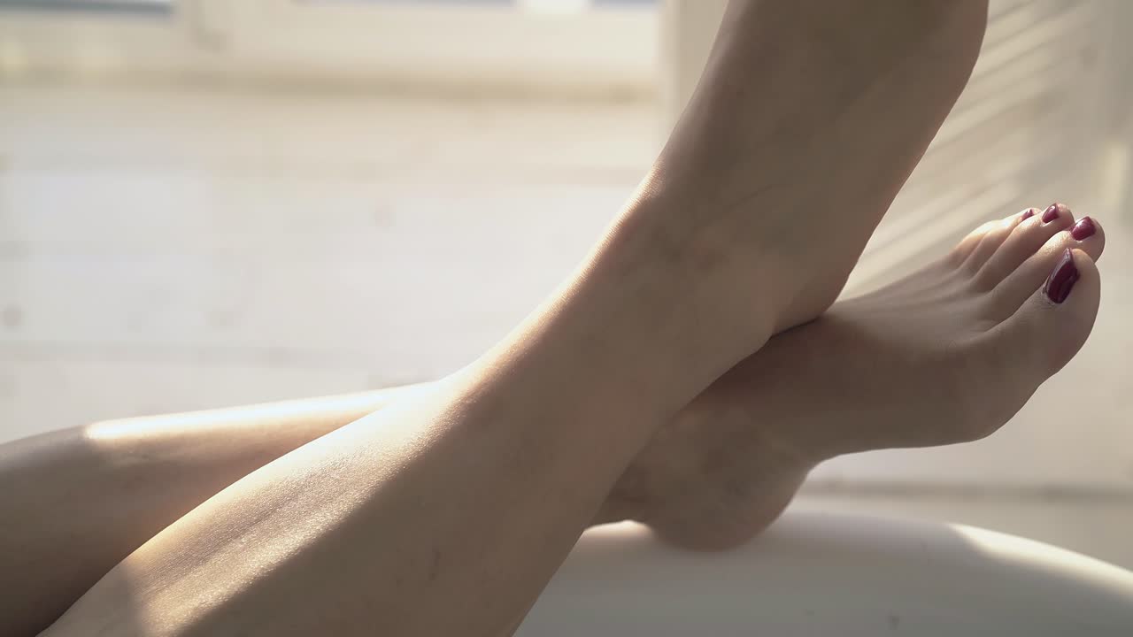 donna in primo piano con i piedi incrociati con un elegante pedicure rosso in bagno