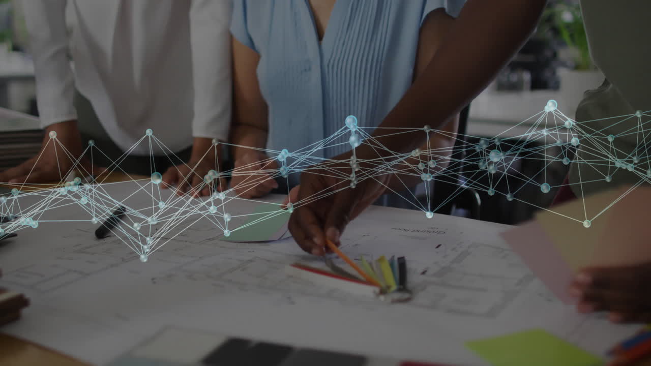 Four designers leaning over blueprints in design studio, displaying floating network graph overlay