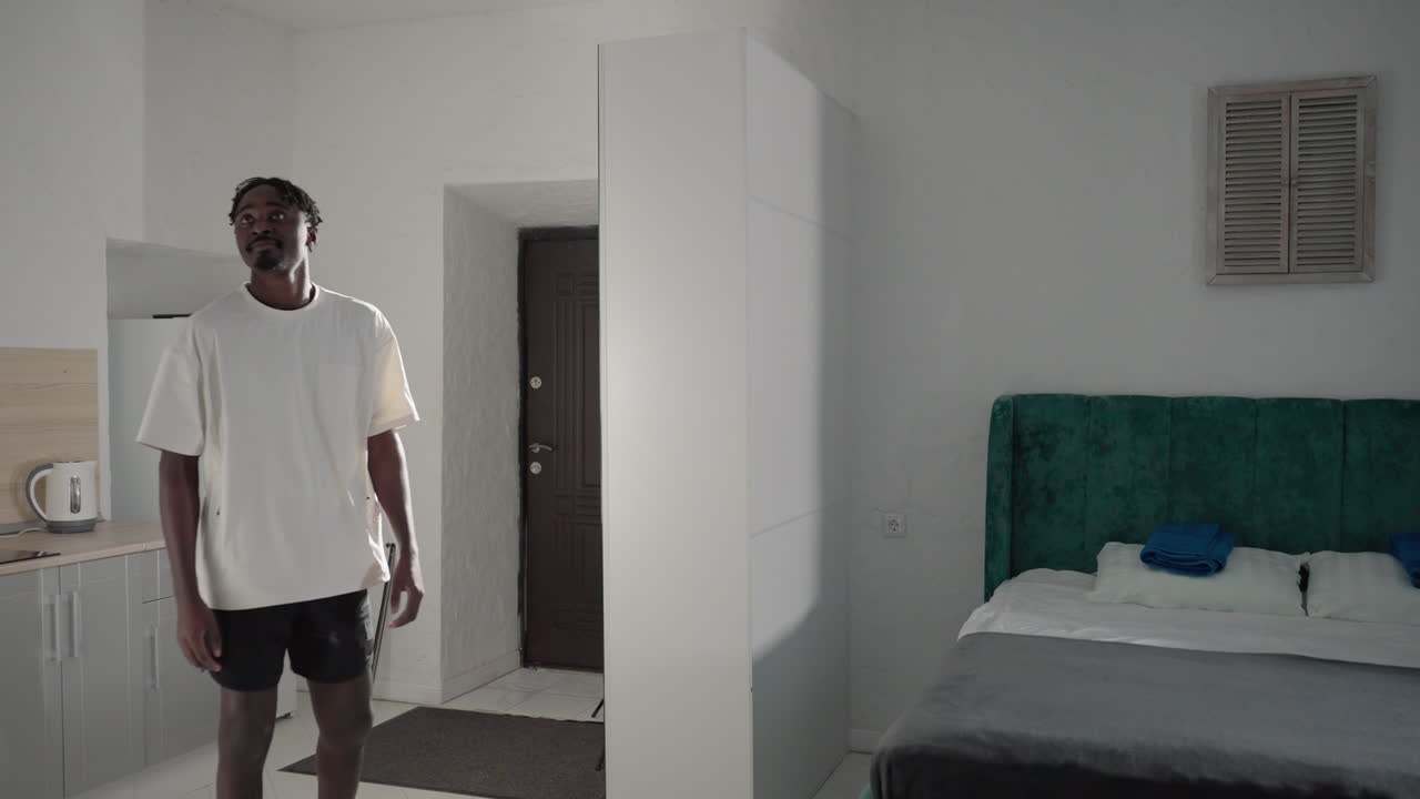 Man with backpack standing in bright, minimalist home interior, looking around curiously, preparing to leave, white walls, simple furniture, doorway with door slightly ajar in the background