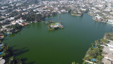 drone video of a lake or lagoon with a small island in the middle surrounded by many houses and trees