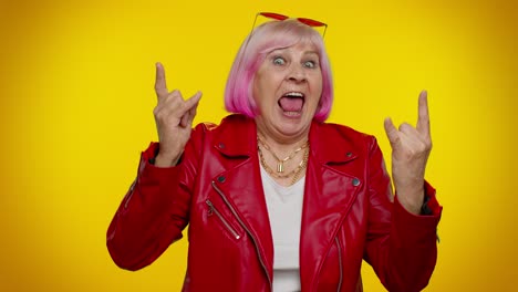 cool senior woman in pink hair and red leather jacket posing with rock and roll sign