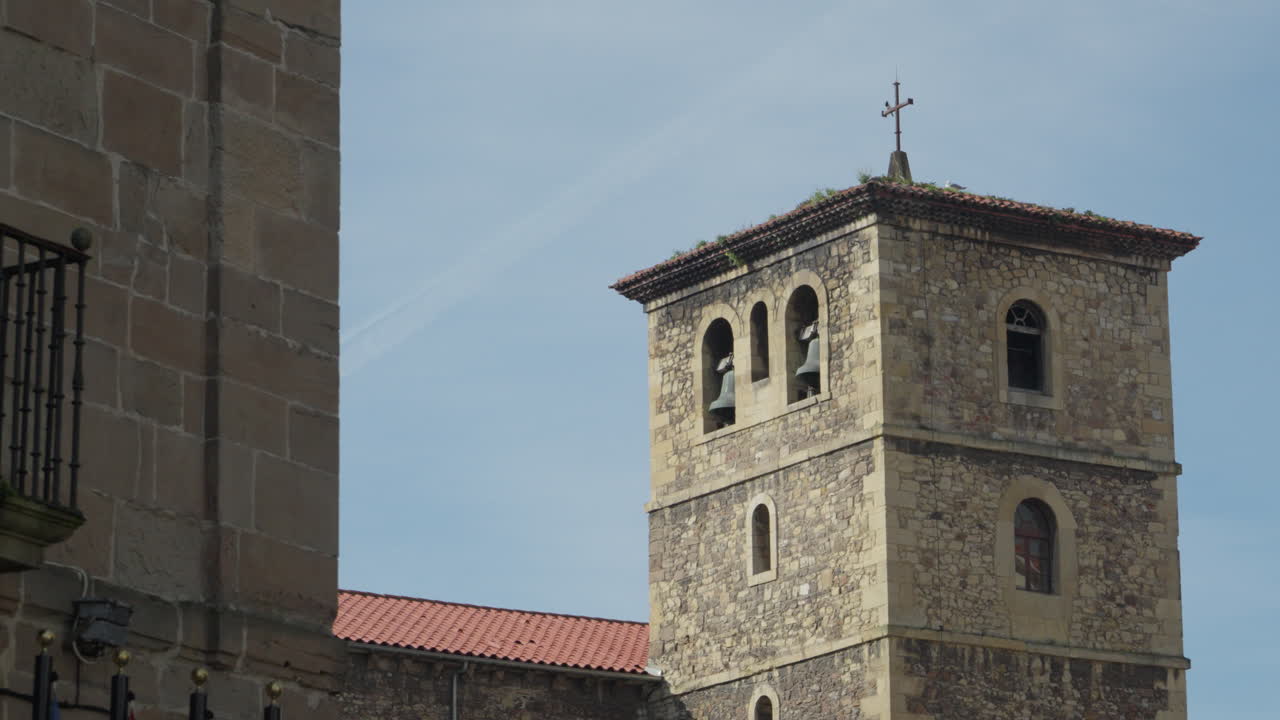 Antico campanile medievale in pietra con finestre ad arco e croce si erge sopra l'architettura storica nel centro storico di Avilés, Asturie, Spagna, sotto un cielo azzurro e limpido.