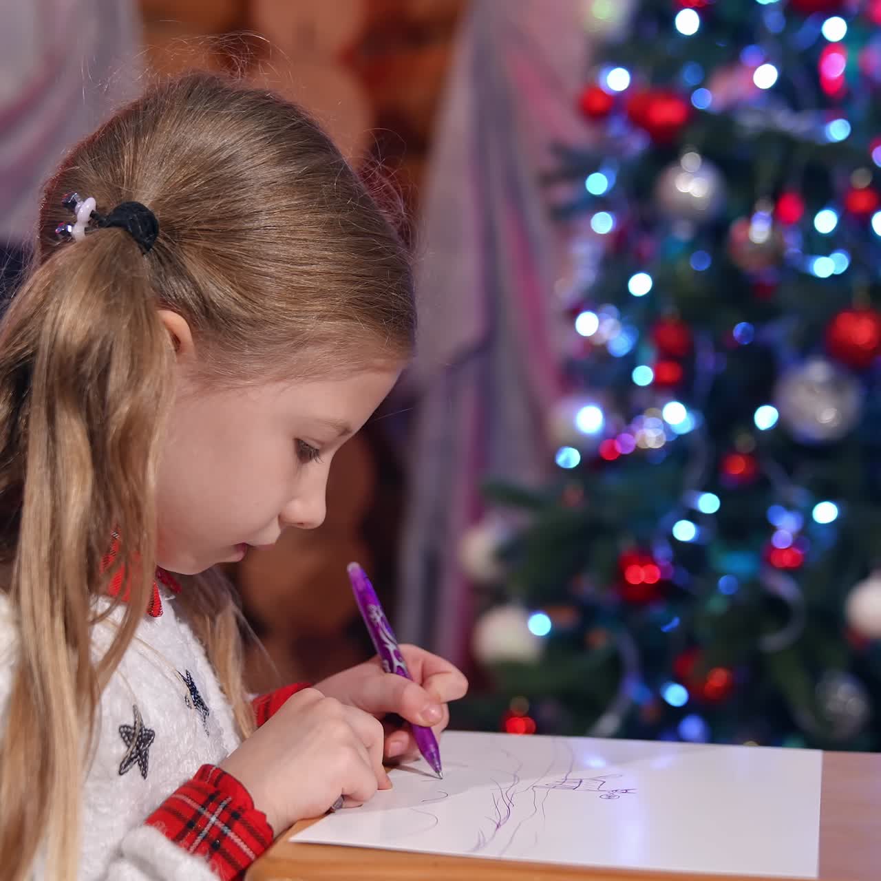 Little girl painting on Christmas tree background. Cute child drawing a picture to Santa before Christmas. New Year tree with bright lights in the room