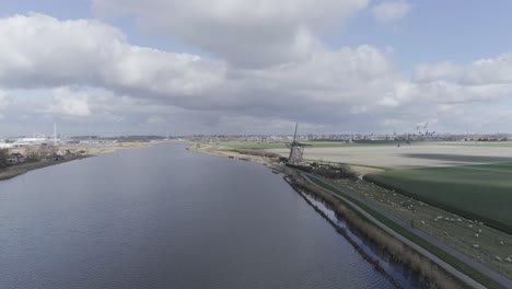 Drone-shot-of-typical-dutch-landscape-with-windmill,-farmland-and-city-in-the-background