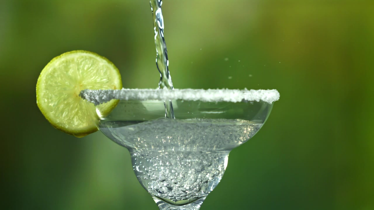 Liquido trasparente rinfrescante versato in un bicchiere da Margarita con bordo di sale e lime