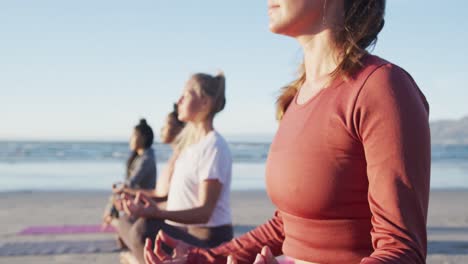 group of diverse female friends meditating at the beach