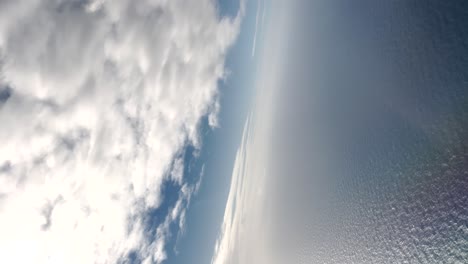 a vertical video captures the ocean and cloudy sky through the window of a flying plane, embodying the concept of travel and vacation