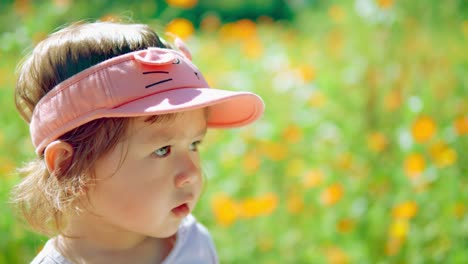 Girl's-face-close-up-looking-with-caution-or-wariness-at-the-flowering-field-on-sunny-day---slow-motion