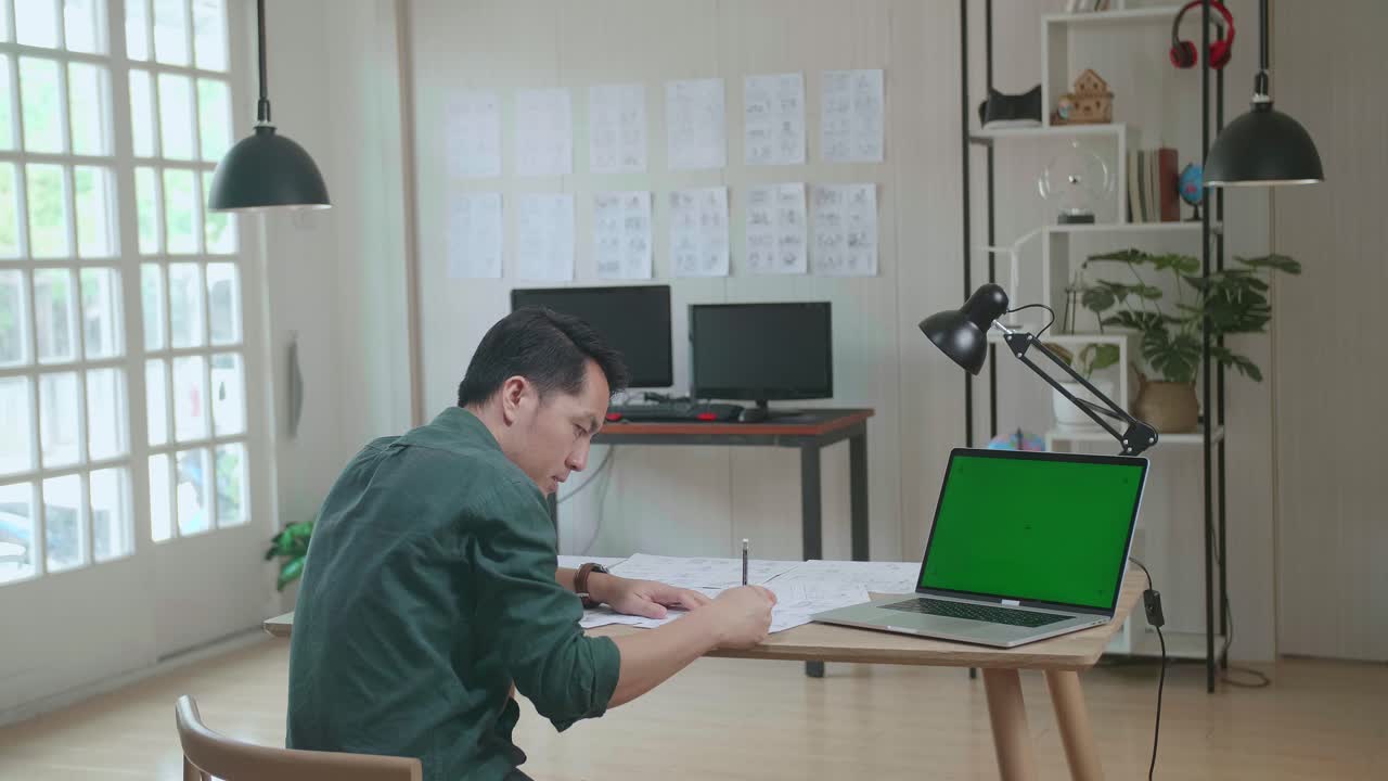 Asian Man Drawing Storyboard Animation Comic Cartoon With Mock Up Green Screen Laptop Computer, Design Creative Scene Layout At Studio. Behind Making Work Before Production Films Or Video Shot