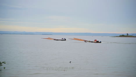 two fishing boats sail at sunrise to catch school of fish on calm sea surface in summer