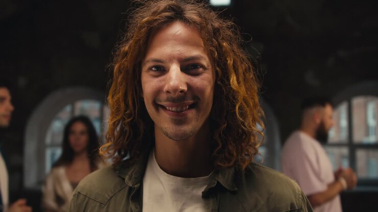 Portrait of a Happy man with curly hair in a Green jacket looking at the camera amid other participants during group therapy. Group therapy client and participant