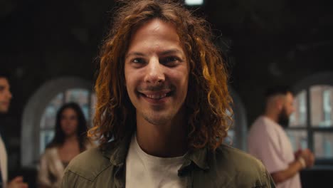 portrait of a happy man with curly hair in a green jacket looking at the camera amid other participants during group therapy. group therapy client and participant