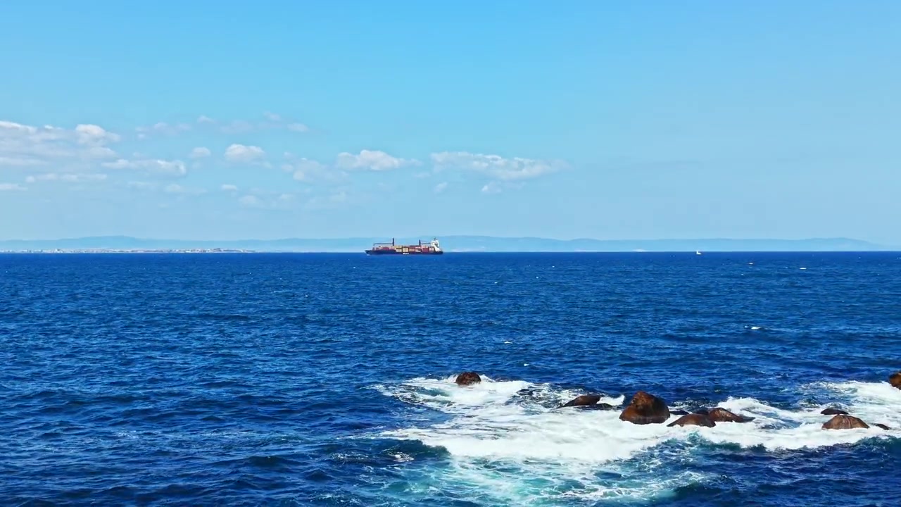 晴れた日、岸辺に波と岩が見える海を航行する船