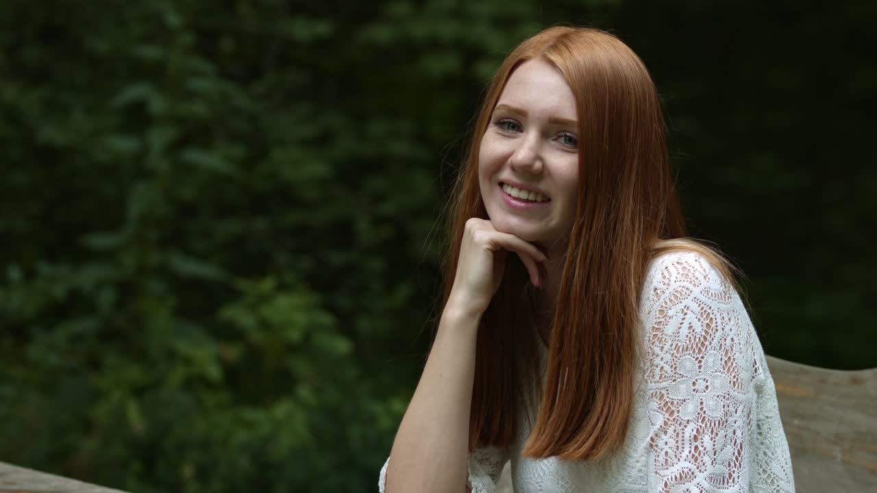 여름 초상화, 아름다운 주근깨가 있는 젊은 여성이 공원에 앉아서 카메라에 미소를 짓고 있습니다.