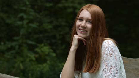 Summer-portrait,-beautiful-freckled-young-woman-sitting-in-park-and-smiling-to-camera