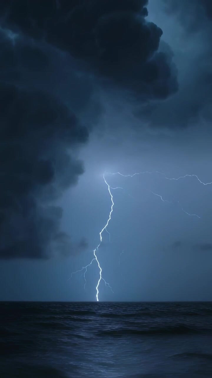 Video verticale: Nuvola temporalesca che rilascia fulmini a zig-zag verso il mare, scaricando energia e illuminando le onde.
