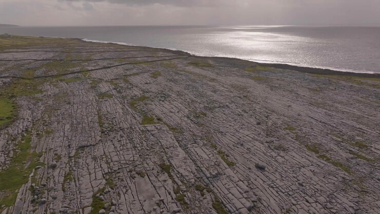 A sweeping aerial shot of the unique karst limestone pavement at The Burren, showing the rugged Atlantic coastline and stone walls in County Clare, Ireland.