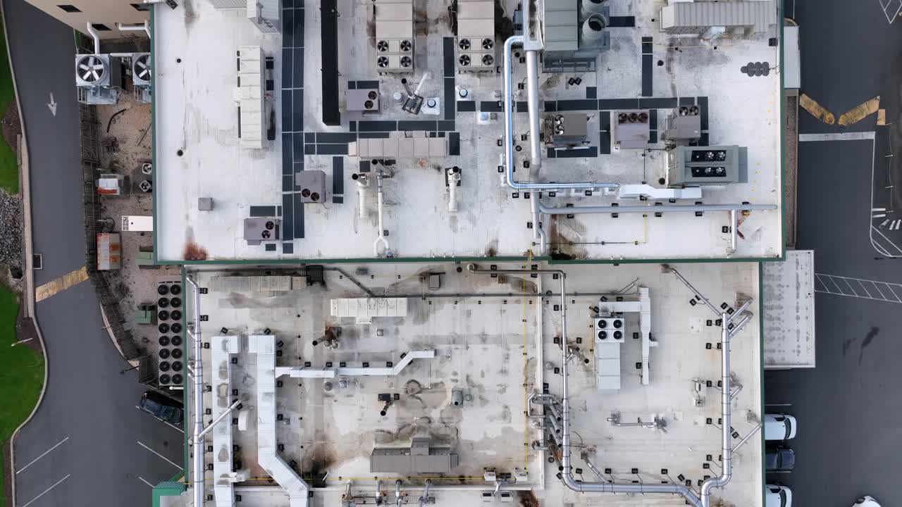 Aerial top view of industrial rooftop filled with HVAC systems and ventilation pipes. Complex layout of machinery and pathways. Urban infrastructure from above. Clean lines and geometric patterns.