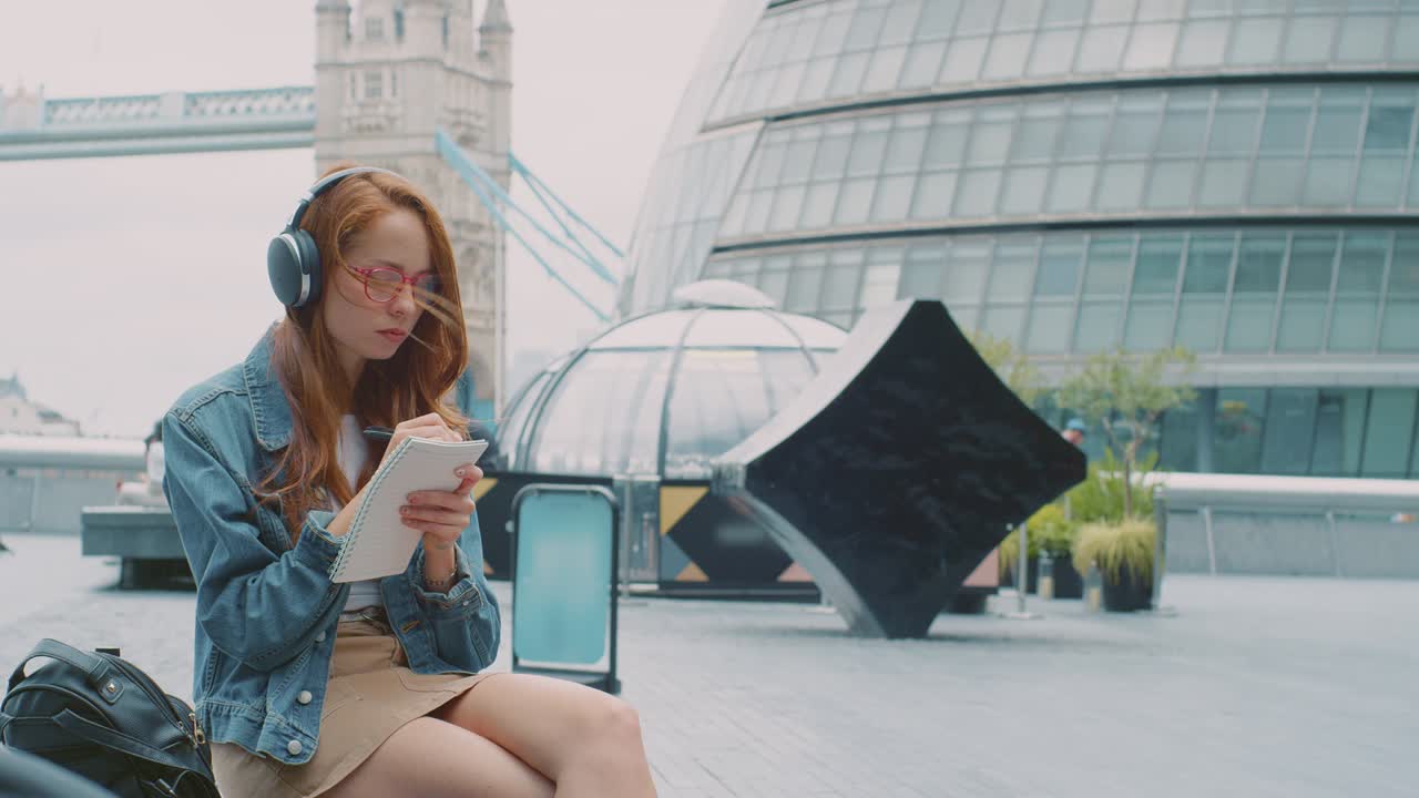 vlogger femenina o influencer social con auriculares viajando por la ciudad tomando notas en un libro