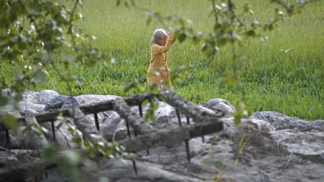 Careless-Little-girl-in-yellow-dress-dancing-on-green-lush-meadow,-Super-Slow-motion-Shot