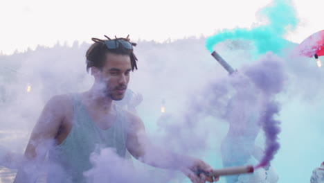 friends holding colored smoke bombs and dancing on lake party