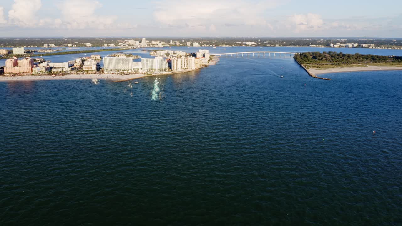 From above, Clearwater Beach stretches beside calm Gulf waters, with a long bridge linking the shoreline to inland waterways and surrounding coastal communities
