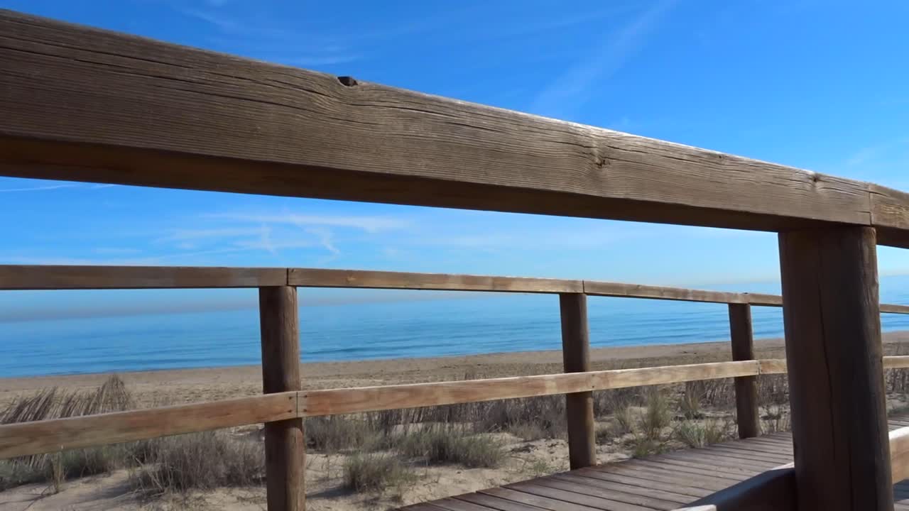 a Slow vertical panning shot of a wooden walkway overlooking the blue ocean and white beach
