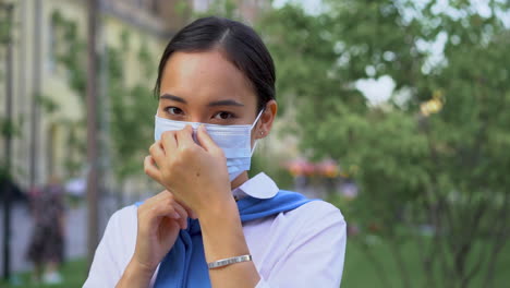 cheerful asian woman putting on medical mask outdoors after coronavirus lockdown. covid-19 pandemic