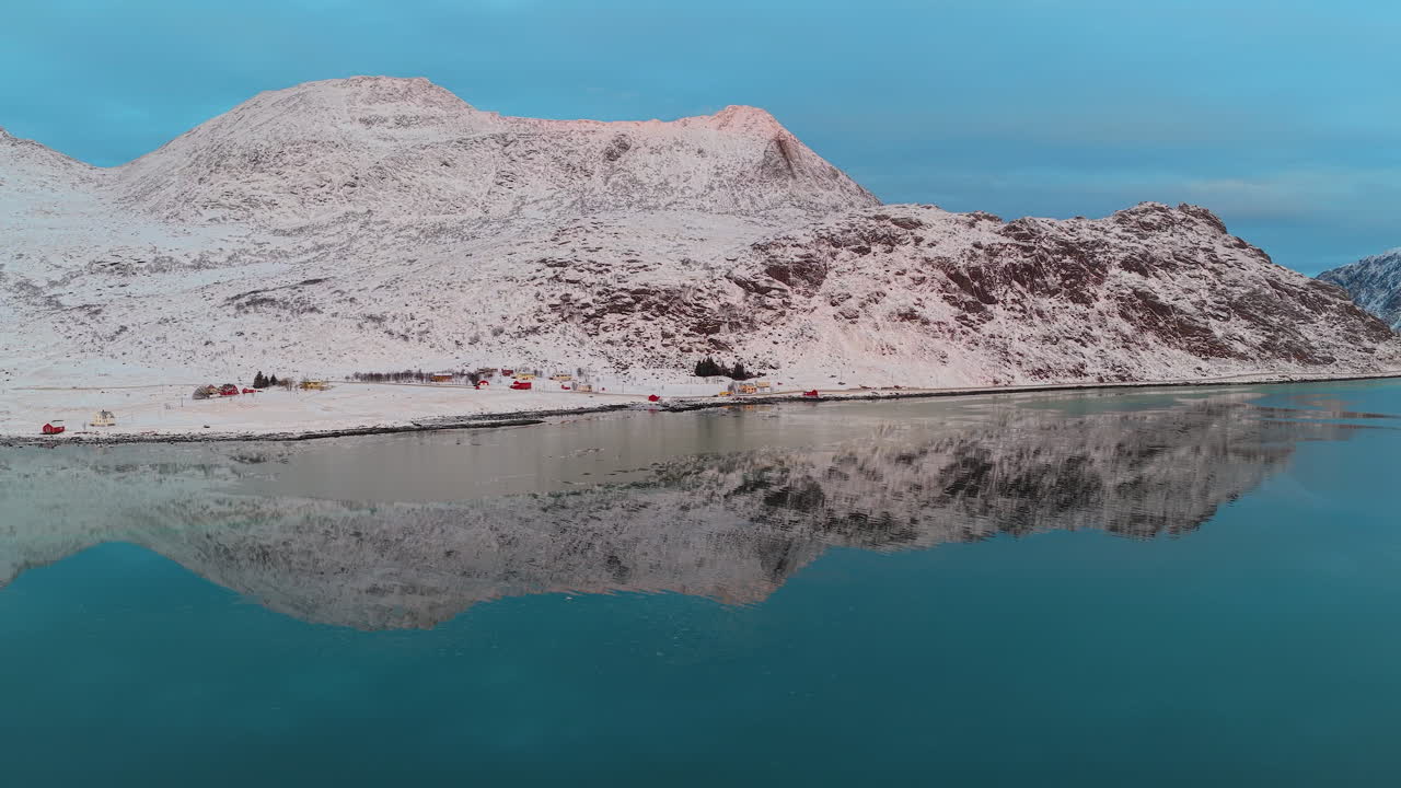 Mozzafiato ripresa aerea di cime innevate riflesse nelle calme acque turchesi di un fiordo norvegese durante l'inverno. Cattura la serena bellezza delle Isole Lofoten.