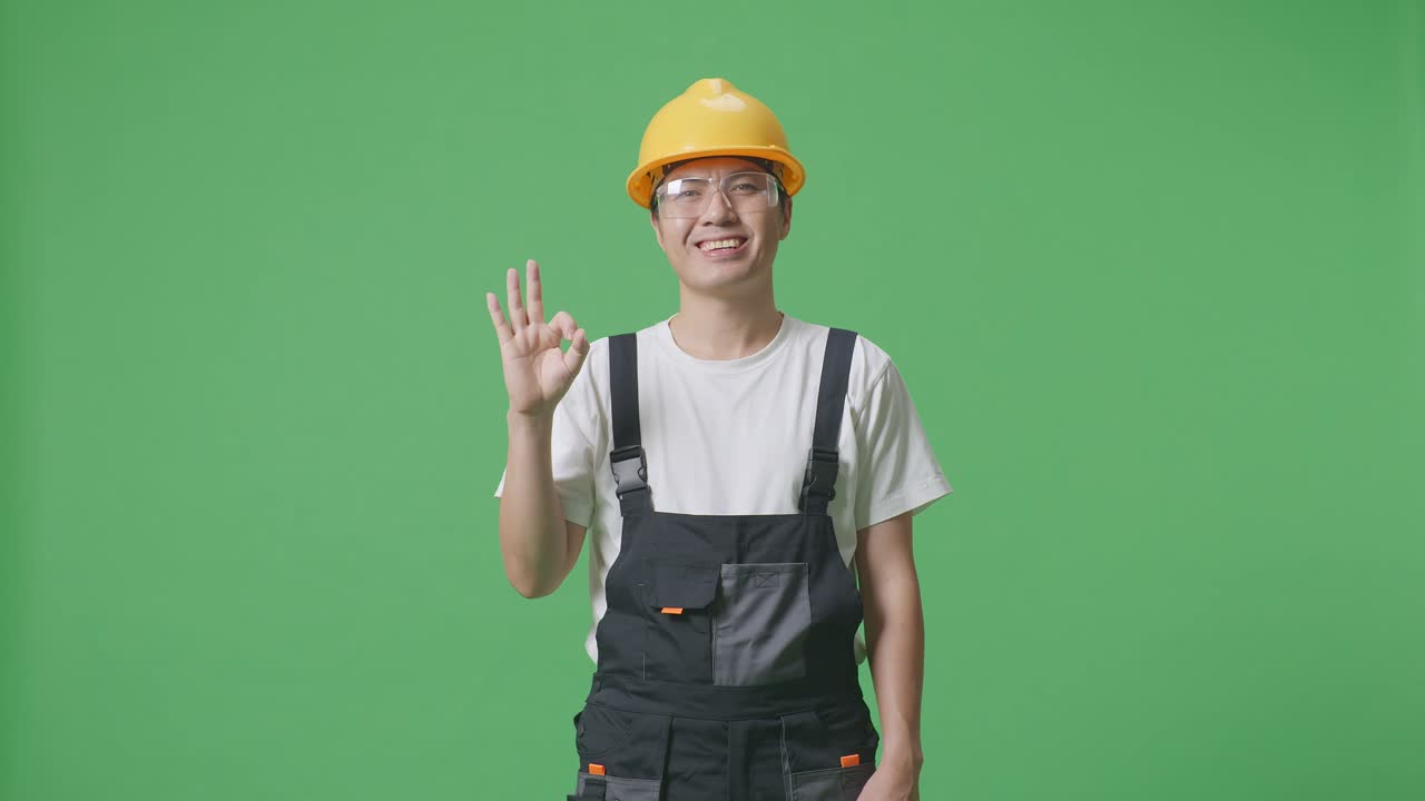 Asian Man Worker Wearing Goggles And Safety Helmet Smiling And Showing Okay Gesture To Camera While Standing In The Green Screen Background Studio
