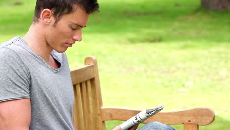 Man-reading-a-newspaper-while-sitting-on-a-park-bench