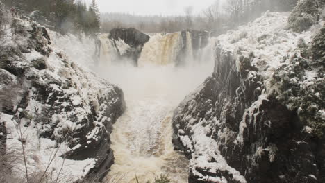 winter panorama of pigeon falls surging from snowmelt, while fresh snow falls against the dramatic backdrop