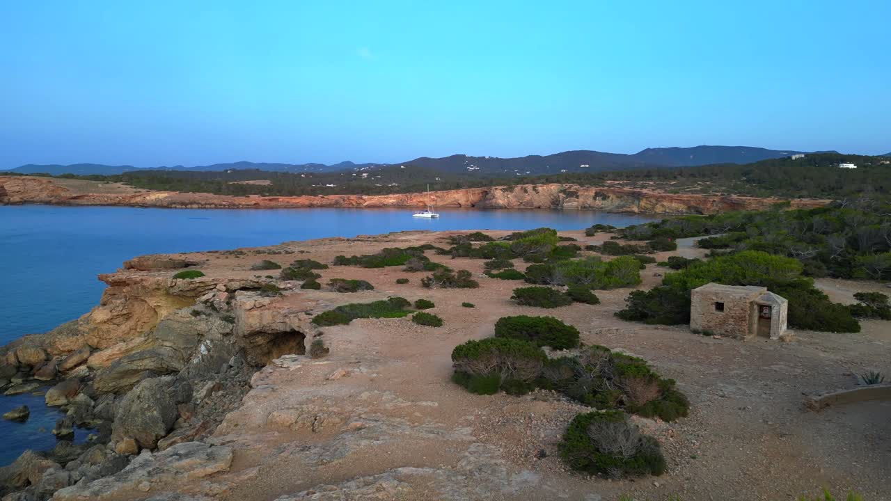 Carefree woman in pink dress with open arms enjoying freedom and breathtaking view on Ibiza island near Torre des Savinar at sunset. Dramatic aerial view flight