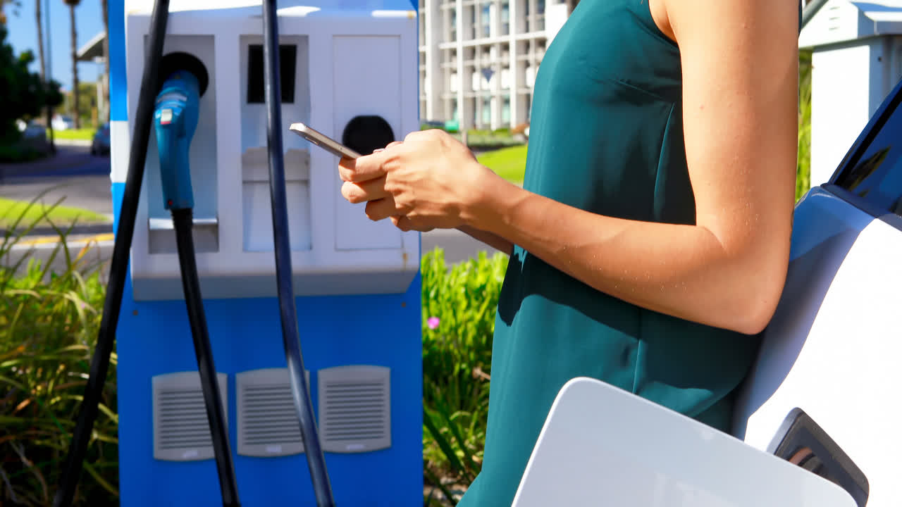 전기 자동차를 충전하는 동안 휴대폰을 사용하는 여성 4k