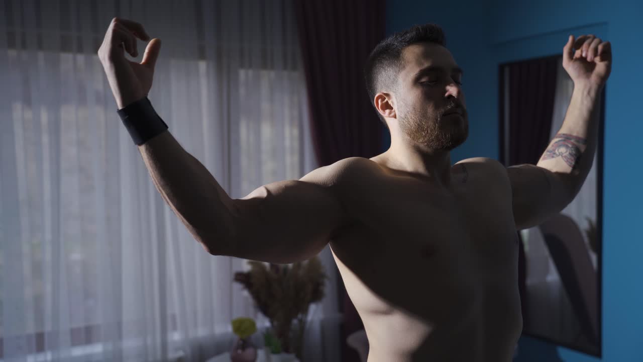크고 근육질의 몸매를 가진 젊은 남자가 집에서 셀프 포즈를 취하고 있습니다.