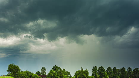 Dunkle-Sturmwolken-Ziehen-über-Eine-Grüne-Landschaft-Mit-Im-Wind-Schwankenden-Bäumen,-Zeitraffer