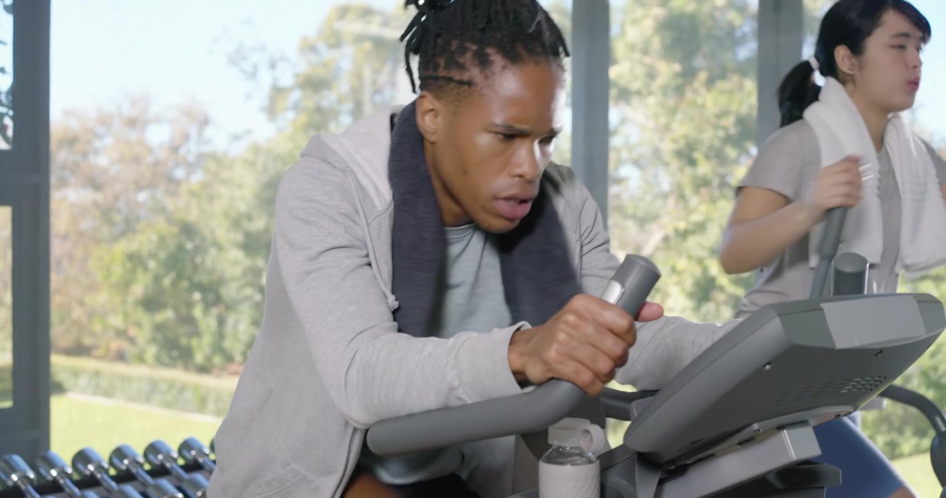 Diverse gym peers using bike and elliptical, bike rider increasing effort during workout session