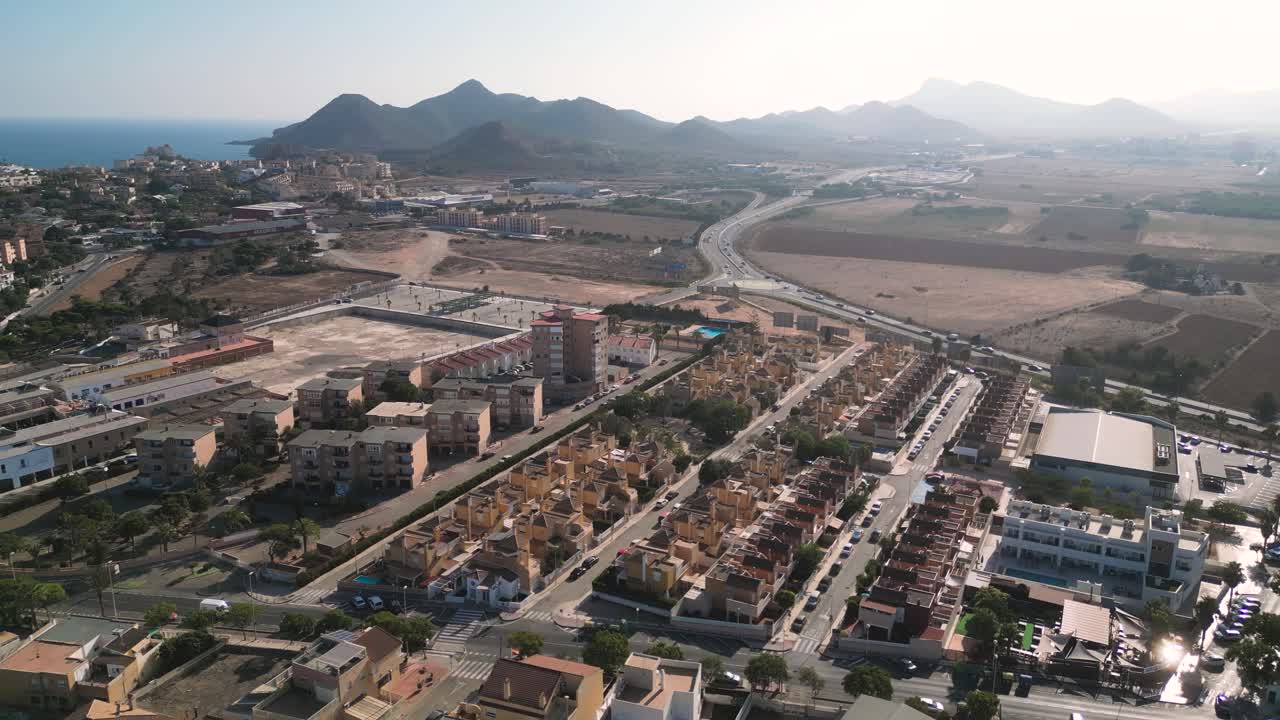 Aerial view of a coastal town of Cabo de Palos in Murcia, Spain. Sunny day, residential buildings, roads, mountains and sea in the distance. Urban meets nature in a scenic Mediterranean landscape.