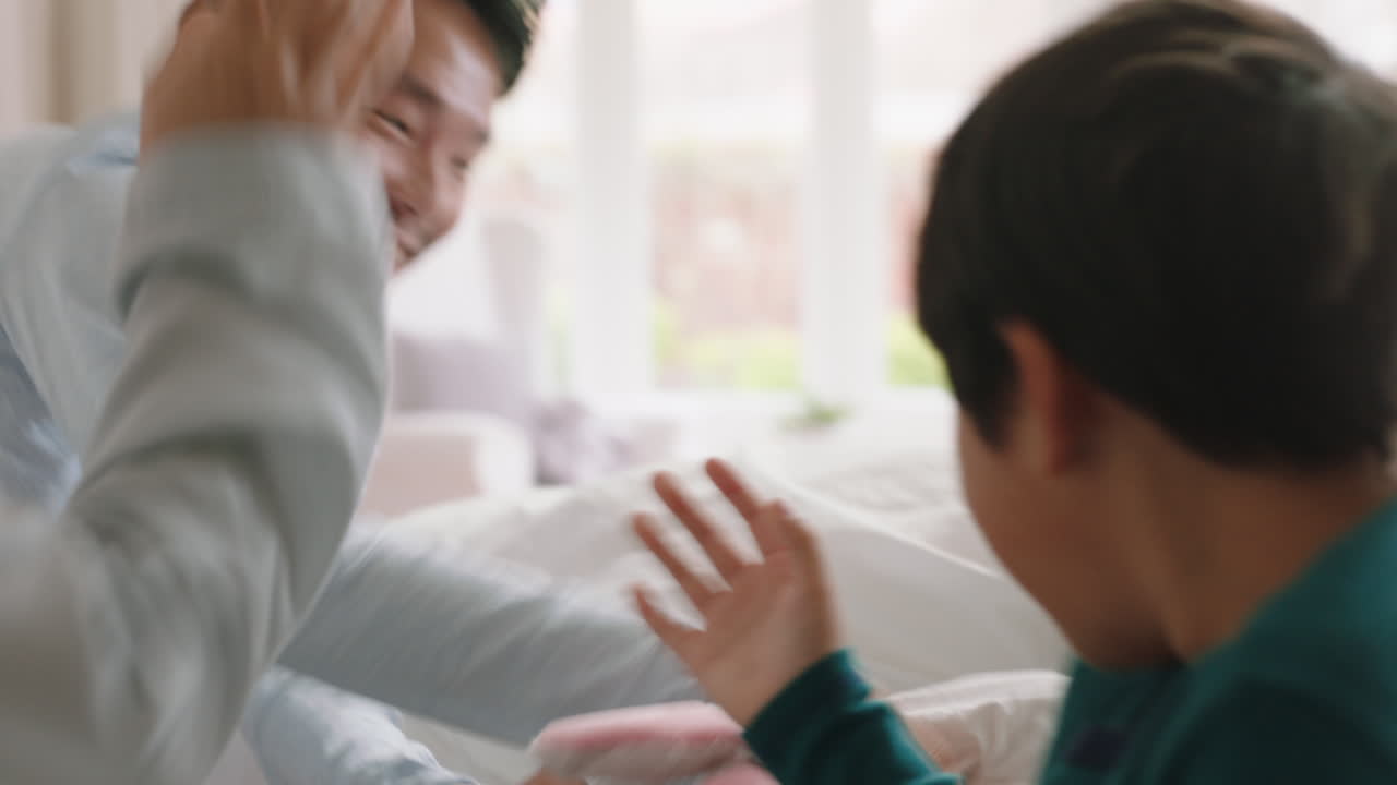 행복한 아시아 가족과 아이들이 침대에 뛰어들고 엄마와 아빠와 함께 놀고 주말 아침에 재미를 느끼고 흥분된 어린 아이들이 부모와 함께 집에서 게임을 즐기고 있습니다. 4k 영상