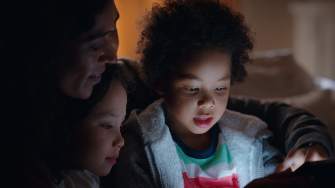 famiglia felice che usa il tablet con i bambini madre e padre che guardano i bambini giocare con la tecnologia touchscreen che si godono una serata rilassante prima di andare a letto