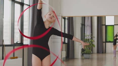 junges mädchen, das rhythmische gymnastik mit einem band in der turnhalle praktiziert