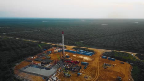 cinematic drone footage of onshore drilling rig equipment structure for oil exploration and exploitation in the middle of jungle surrounded by palm oil trees during sunset and high oil price