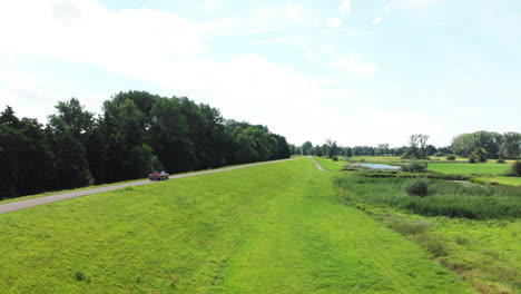 Red-Cabriolet-Car-Driving-And-Travelling-On-The-Road-With-Green-Hills-At-Daytime-In-Zwolle,-Netherlands