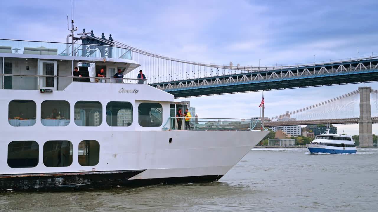 Riverboats move towards each other by the East River. Low angle view on the Manhattan Bridge and Brooklyn Bridge at the backdrop of cloudy sky
