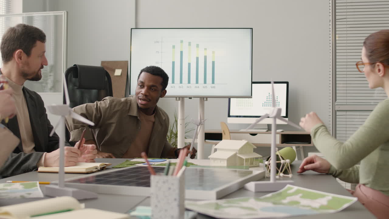 Man Explaining Wind Turbine Model And Showing Data Graph During A Meeting In The Office