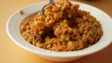 closeup of a bowl of bulgur with tomatoes, green peas and red pepper