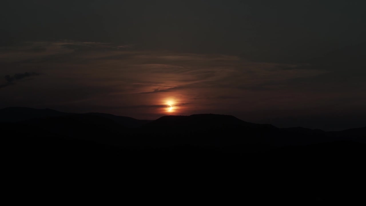 Darkened sky as the sun is partially obscured over distant hills during eclipse