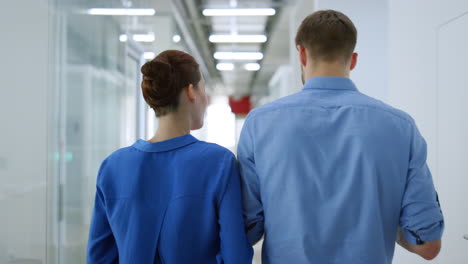 back view man woman walking office. serious business couple talking corridor