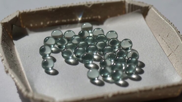 Panning camera approaching glass bead cluster in cardboard tray under bright light