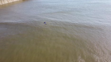 hombre nadando en un océano frío mientras usa un sombrero y guantes